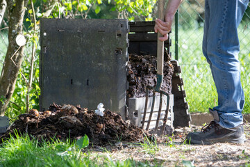 Homme avec une fourche creusant un bac à compost de jardin extérieur rempli de déchets alimentaires. Promouvoir le recyclage durable et les pratiques de compostage domestique.