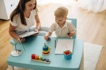 Doctor is teaching the kid. Speech therapist is with young boy indoors