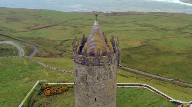 Rhythmic aerial shot of Doonagore Castle in Doolin, with its iconic tower set against a moody coastal backdrop