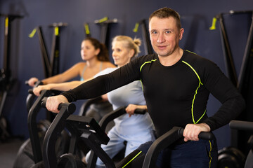 Portrait of positive concentrated adult man doing cardio training, cycling on stationary bike in...