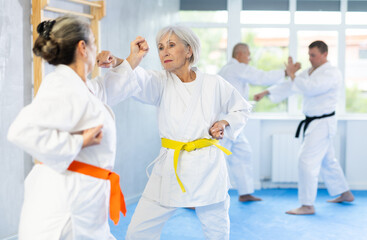 Active old woman attendee of karate classes practicing fighting techniques during workout session