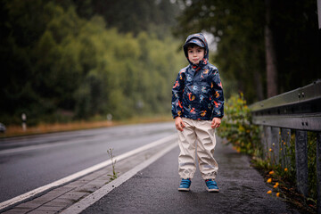 Young Boy Standing on Wet Roadside in Rain Gear