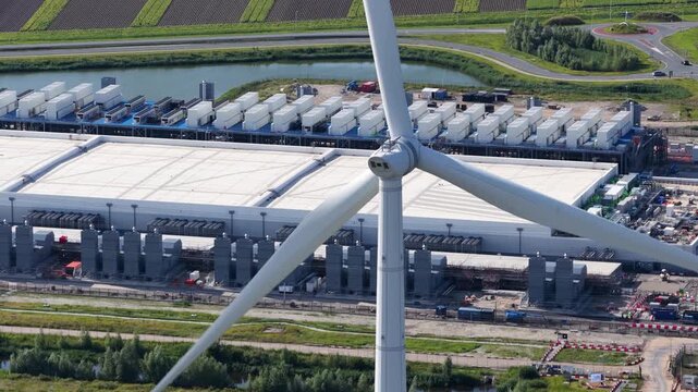 Aerial view of a wind turbine in front of a data center in the Eemshaven, clean energy, energy efficiency, and digital infrastructure - Powered by Adobe