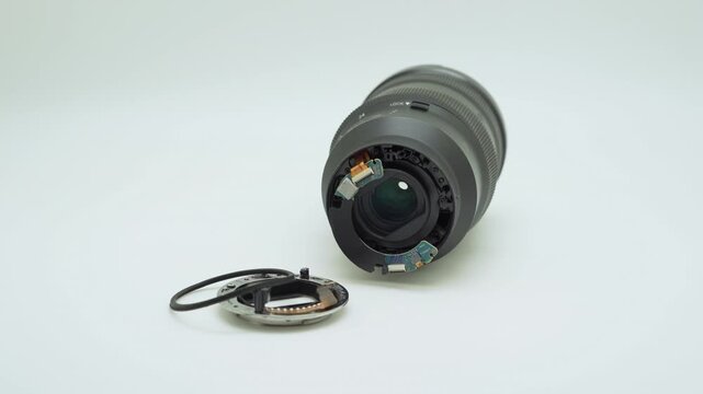 Close-up of a damaged camera lens showing the broken bayonet mount and exposed internal components on a white background.