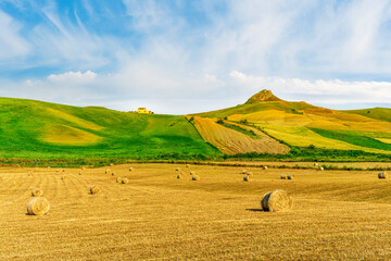 Scenic view at picturesque golden sunset valley in a green shiny field with hay stacks, bright cloudy sky , golden sun rays and beautiful hills on background, summer valley landscape