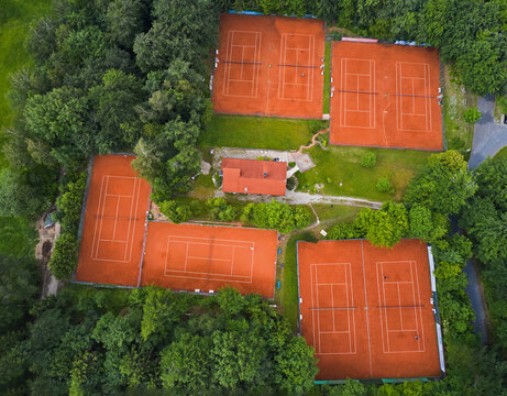 Aerial view of a cluster of red clay tennis courts nestled amidst the dense green foliage of Ebersberger Forst, Ebersberger Forst, Bavaria, Germany.