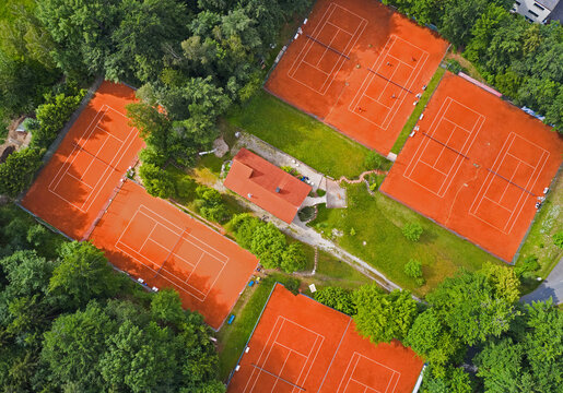 Aerial view of vibrant red tennis courts nestled amidst a sea of deep green foliage, a tranquil oasis of sport and nature, Ebersberger Forst, Bavaria, Germany.