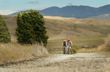 Two people riding on gravel bike track in strong wind. Otago Central Rail Trail. South Island. New...