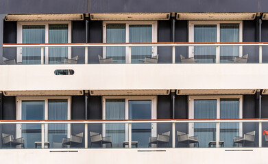 side of a cruise ship with balconies and deck chairs. Cabin windows with tables and seats on the outboard side of a cruise ship