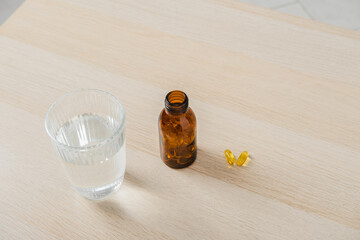 Omega-3 fish oil capsules in transparent bottle and a glass of water stands on the table
