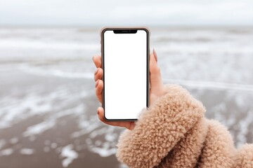 A woman stands on a beach with a cell phone held in her hand