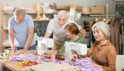 Elderly man teacher shows group of elderly men and women how to sew on sewing machine in class
