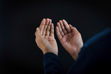 A close-up, over-the-shoulder shot of a man, with hands raised in prayer or supplication against a...
