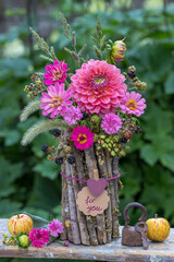 Blumenstrauß mit pink Dahlien, Zinnien, Brombeerzweigen uns Gräsern in einer Zweig-Vase