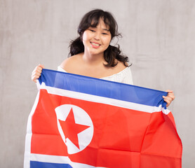 Portrait of smiling young asian girl in casual clothes holding North Korea flag in studio