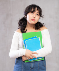 Portrait of pensive asian girl in casual clothes posing with notebooks in studio