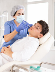 Obraz premium Cosmetologist in medical scrubs, cap and gloves giving filler injection to young man