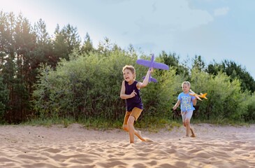 cute caucasian boys running along beach holding toy planes