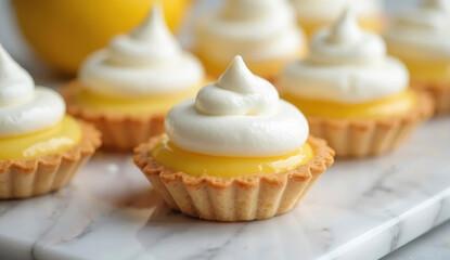 Lemon tarts with glossy yellow filling and fluffy whipped cream peaks are beautifully arranged on a light marble surface. Fresh lemons in the background enhance the vibrant presentation