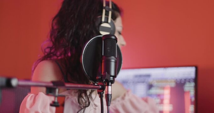 Female music producer in studio with audio recording and monitoring equipment. Girl with headphones in front of professional microphone