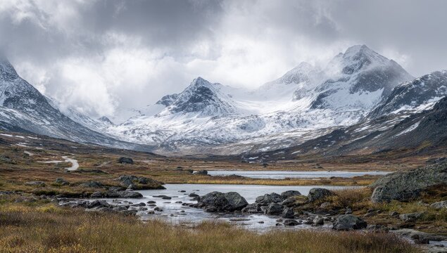Mountainous landscape with lake and snow-capped peaks under a dramatic sky