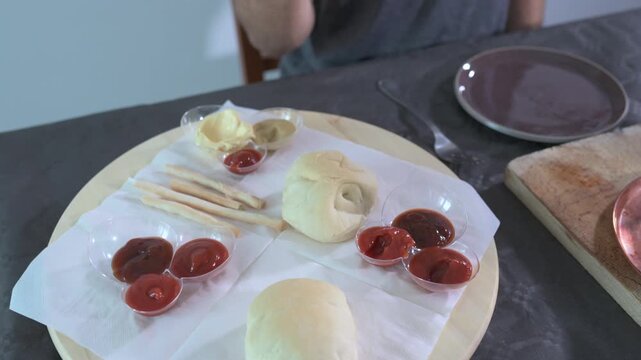 Close-up shots of a circular tray with bread, breadsticks, and sauce containers. A hand with a skewer dips a piece of Bourguignonne meat into the red sauce. A lifestyle of consuming delicious food.