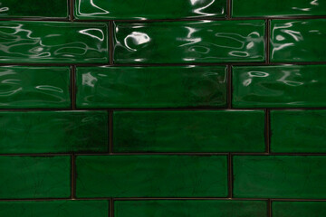 Rich green ceramic tiles create a vibrant and glossy wall surface in an indoor setting, enhancing...