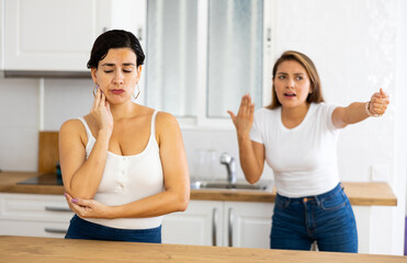 Unhappy offended young Latina standing in kitchen at home, listening to her disgruntled female...
