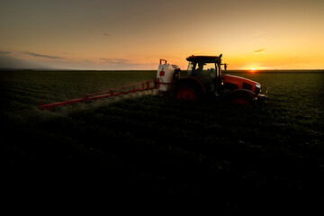 Tractor spraying crops in a lush green field at sunset.