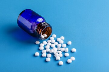 Medicine Pill Bottle Spilling White Round Pills on a Solid Blue Background