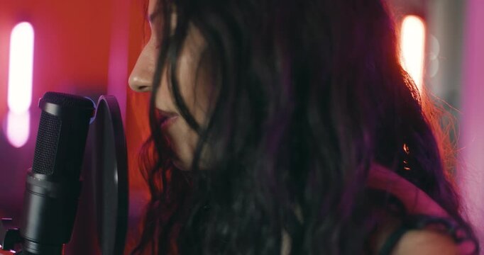 Girl singing on a professional studio microphone. Female music producer with headphones in studio with audio recording equipment. Making a song. Colorful lights.