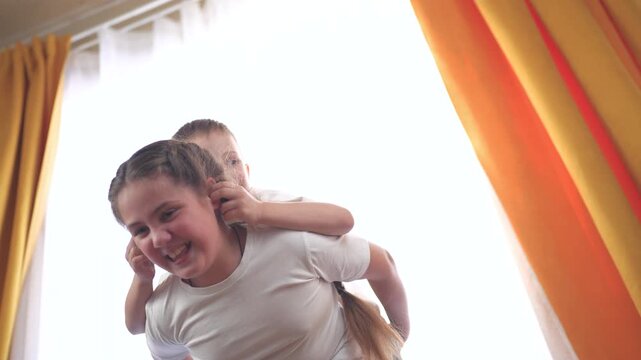 Young boy and little girl sitting on bed. Brother and sister play back roll. Child pulls out pair of ears from a play room. A young boy and lifestyle a small girl are seated on a bed.