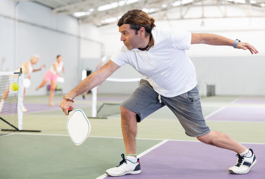 Sporty man pickleball tennis player trains on the indoor court using a racket to hit the ball