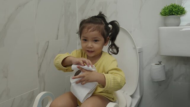 happy toddler girl is sitting on the toilet with tissue at home. potty training and learning