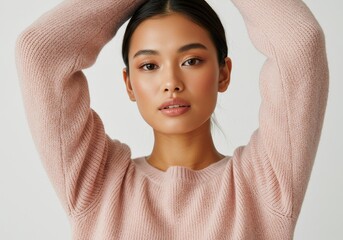 Attractive young woman in a soft pink knit sweater poses with arms raised.
