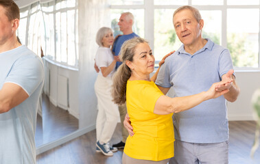 Positive senior woman and man practicing tango dance moves as a couple during a group celebration...
