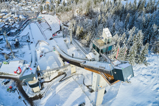 Aerial view of the stark white snow blankets the ski jump complex, contrasting sharply with the dark green of the surrounding forest, Oberstdorf, Bayern, Germany.