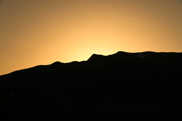 Silhouette of a mountain at golden sunset, powerful calm, warm colors.