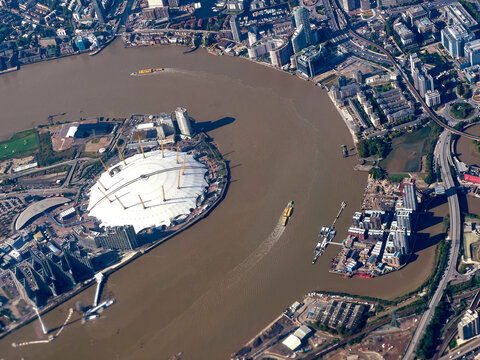 Aerial view of the iconic O2 Arena dome reflecting the sunlight amidst the winding, muddy River Thames, surrounded by the urban sprawl, London, England, United Kingdom.