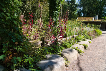 A well-kept garden with a stone path, lush vegetation, and red blossoms.