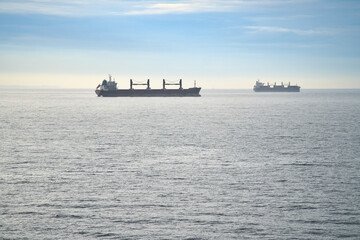Two cargo ships glide across a calm sea under a clear sky. Minimalist seascape.
