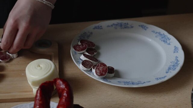 Plating fuet salami, a savory cured meat delicacy. Unhealthy snack arranged on a plate in the kitchen. Close-up of the dish, woman's hands in frame