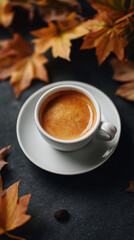 Warm coffee in a white cup surrounded by autumn leaves on a dark surface creating a cozy atmosphere