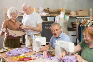 Relaxed interested older adults gathering at sewing course in small studio, cutting fabric, pinning...