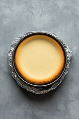Top view of whole New York cheesecake in a round pan lined with foil, even golden edge.