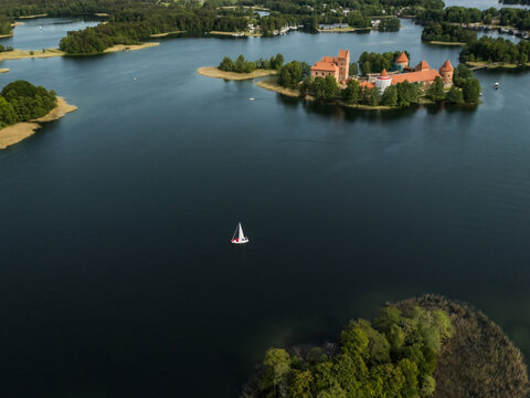 Aerial view of Trakai Island Castle, a medieval castle, stands in stark contrast to the dark water, with a lone sailboat nearby, Trakai, Vilnius country, Lithuania.