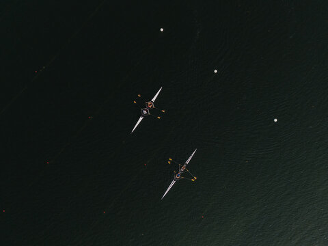 Aerial view of two rowing boats slicing through the dark, rippled waters of the lake Galve, their oars creating fleeting white splashes against the somber surface, Trakai, Vilnius country, Lithuania.