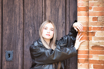 young and beautiful blonde woman in black leather jacket, boots and short skirt rests her two hands...