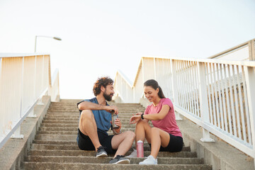 A couple takes a break while enjoying drinks after exercising on outdoor stairs. The warm morning...