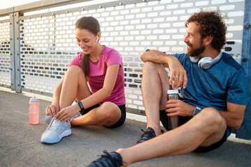Two active individuals take a break from their workout on a sunlit bridge, chatting and enjoying...
